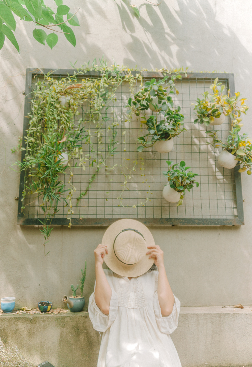 Woman Wearing White Dress Leaning on White Wall Covering Her Face With Brown Hat